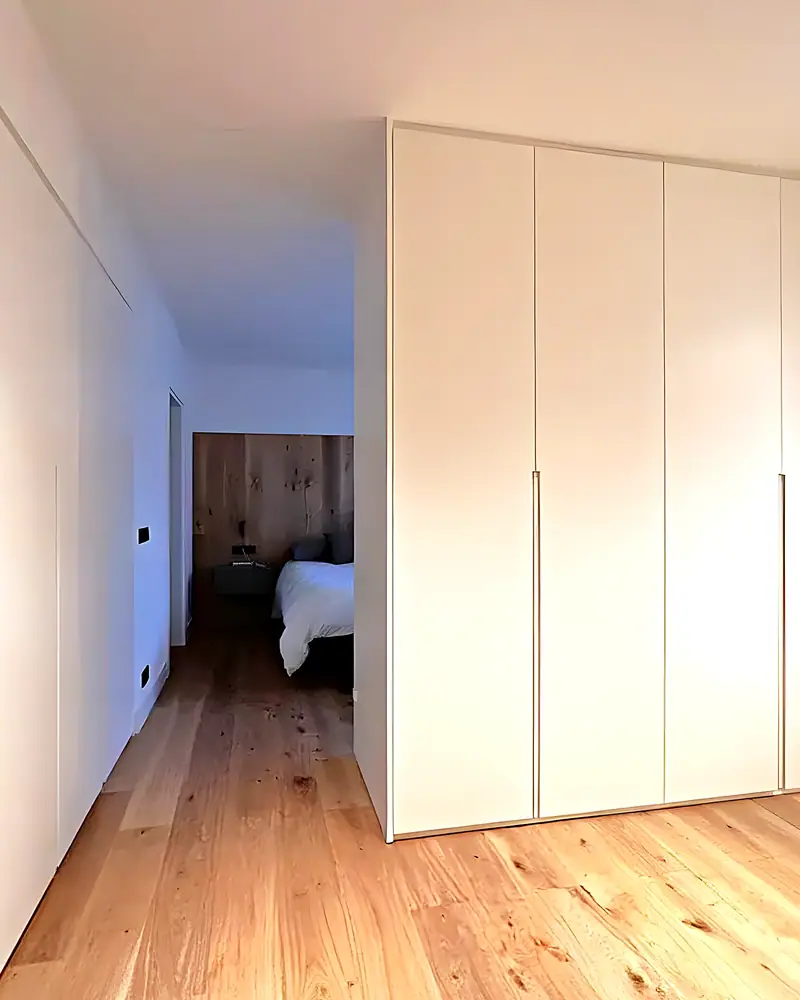 Armarios lacados blancos con nicho de madera y vista del pasillo al dormitorio