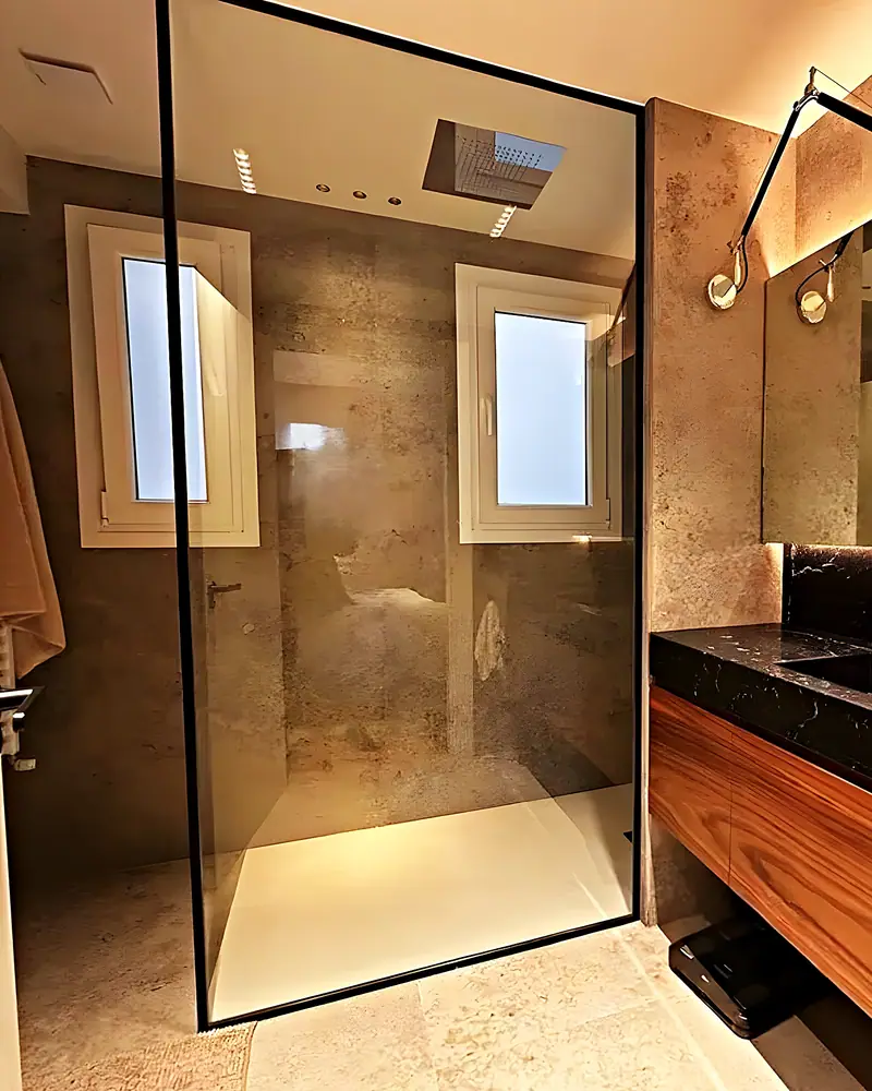 Baño con ducha de obra, mampara de perfil negro, encimera de mármol negro y mueble de nogal