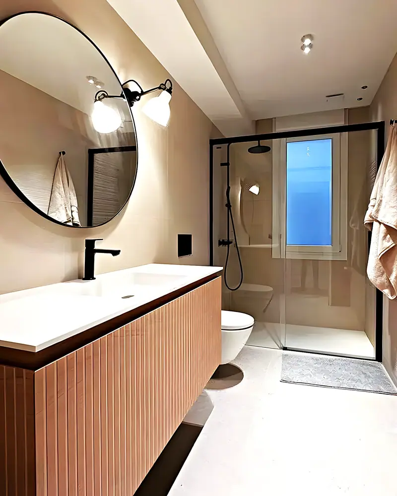 Baño con mueble acanalado en terracota, espejo redondo y ducha con ventana al fondo