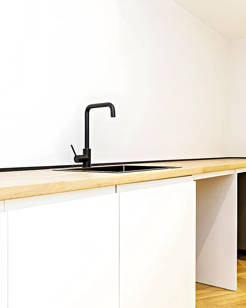 Encimera de madera con fregadero y grifo negro sobre muebles blancos