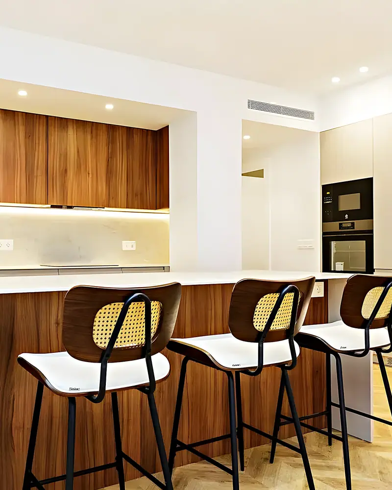 Cocina reformada con isla de nogal, taburetes de rejilla y suelo de madera en espiga