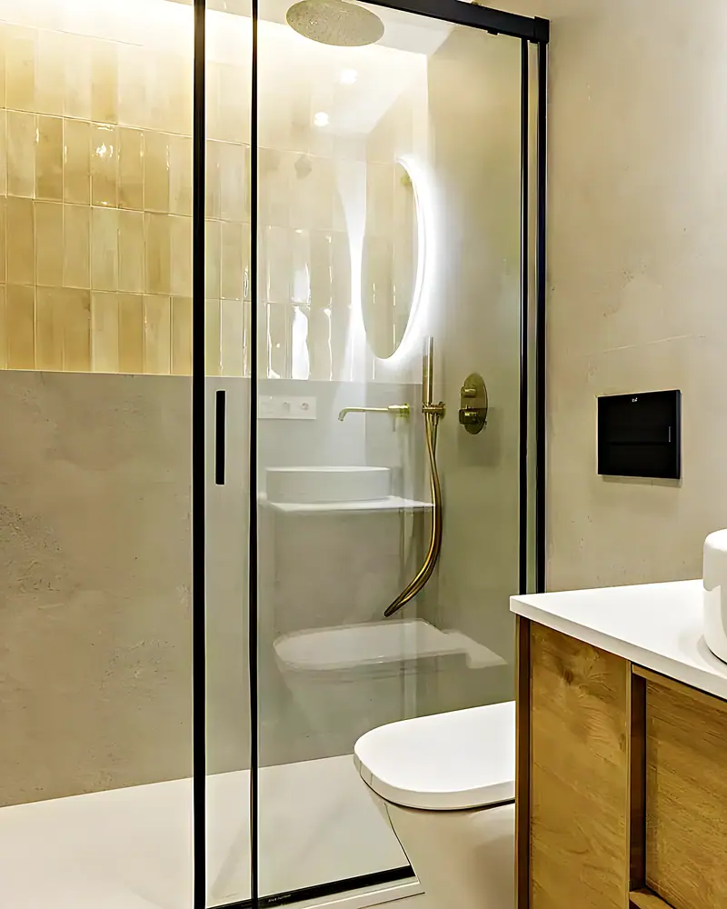 Ducha con azulejo artesanal ámbar, grifería dorada y lavabo sobre mueble de madera