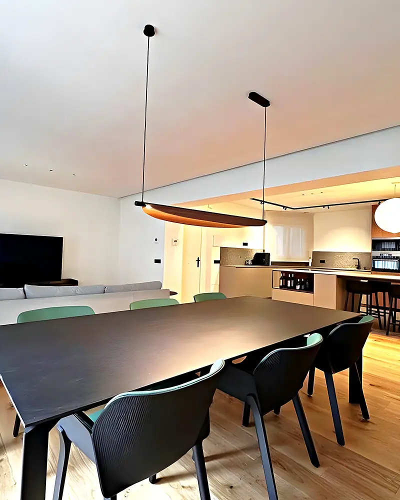 Salón-comedor abierto a la cocina, con mesa negra, sillas verdes y suelo de roble